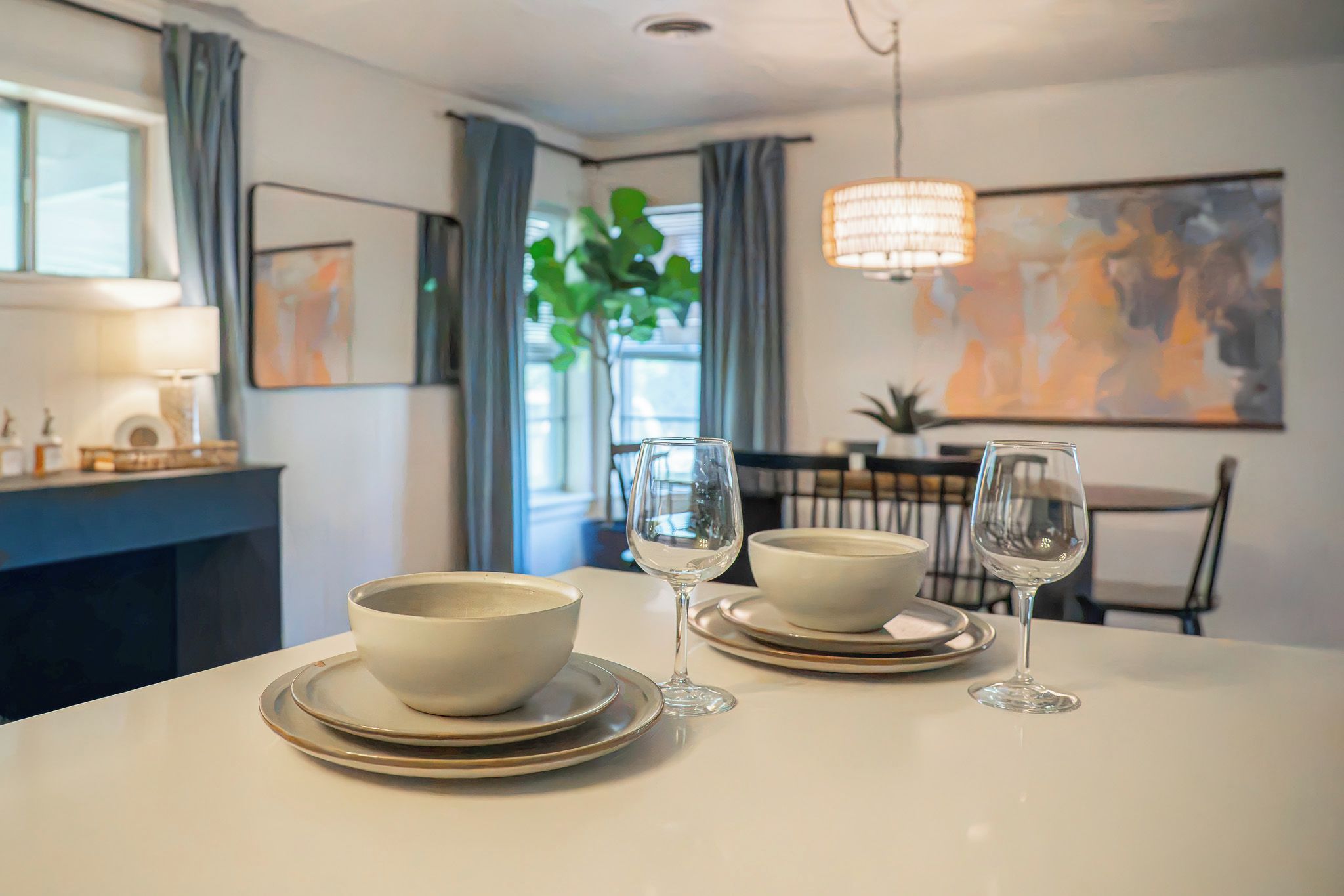 Une table à manger avec deux bols et deux verres à vin, une lampe et un tableau accroché au mur.