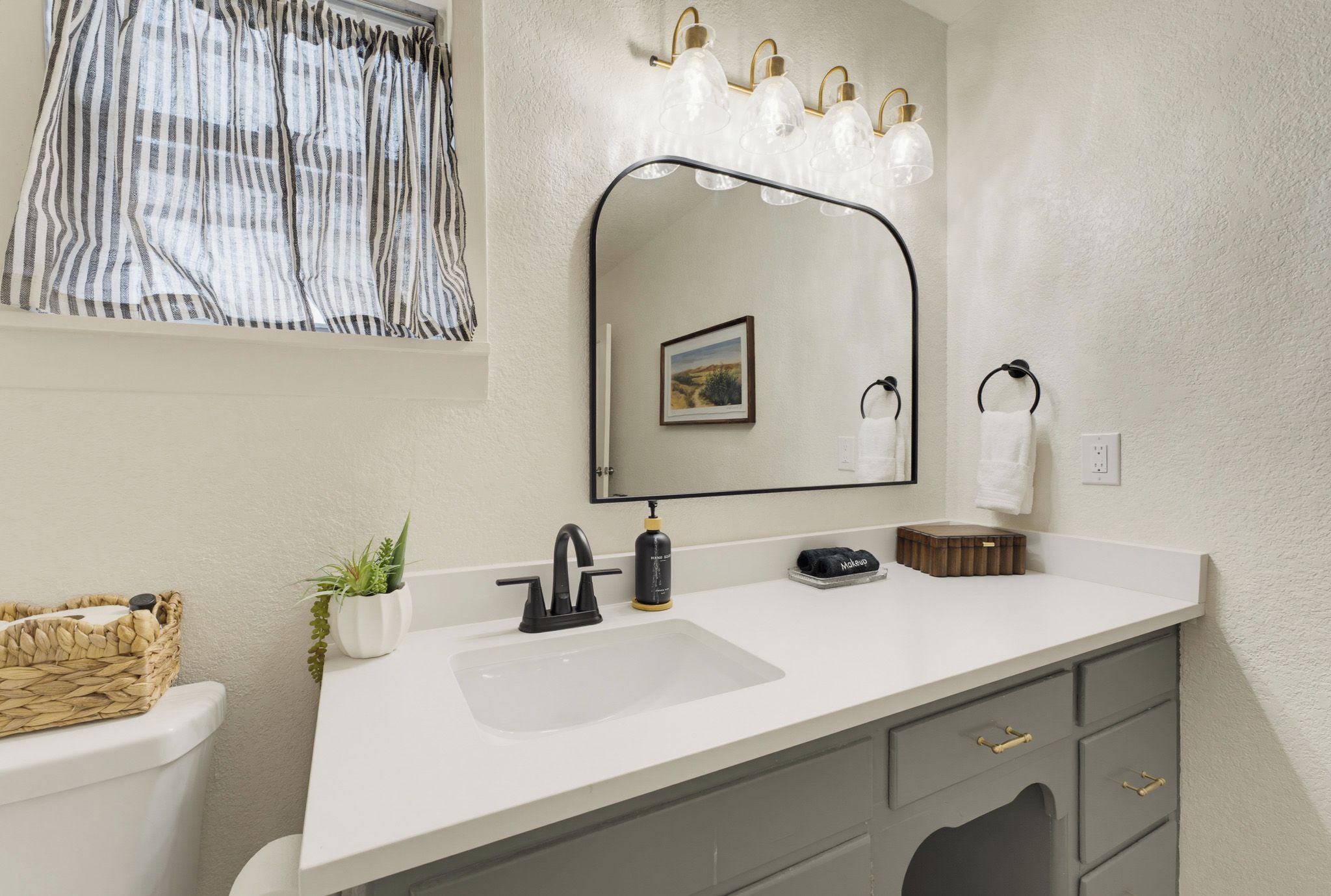 Une salle de bain avec un lavabo blanc, un miroir avec éclairage intégré, un porte-serviettes et une petite plante.