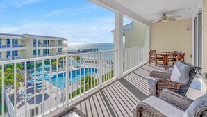 Ein Balkon mit Blick auf Pool und Meer, mit Korbmöbeln und Deckenventilator.