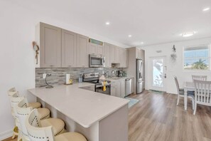 A modern kitchen with white cabinets, a central island, and a dining area with a white table and chairs. - *NEW* Coral Sands Oceanfront-Beach & Pool (Key Colony Beach)