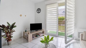 A modern living room with a flat-screen TV, a wooden entertainment unit, a potted plant, and a sliding glass door leading to a balcony.