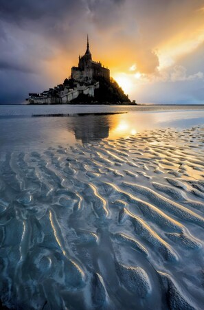 A castle on an island with a calm sea in the foreground.