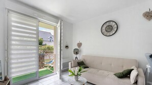 A modern living room with a sliding glass door, a beige sofa, a small round table with a plant, and a wall clock.
