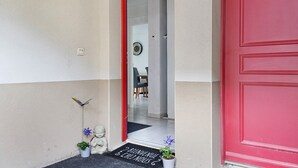 A red door, a welcome mat, a small potted plant, and a wall-mounted light fixture.