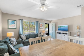 A living room with a sofa, a dining table, a ceiling fan, and a television. - Sandprints D3 (Miramar Beach)