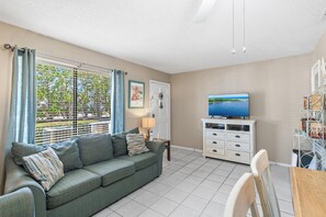 A living room with a sofa, TV, and a dining area with chairs. - Sandprints D3 (Miramar Beach)