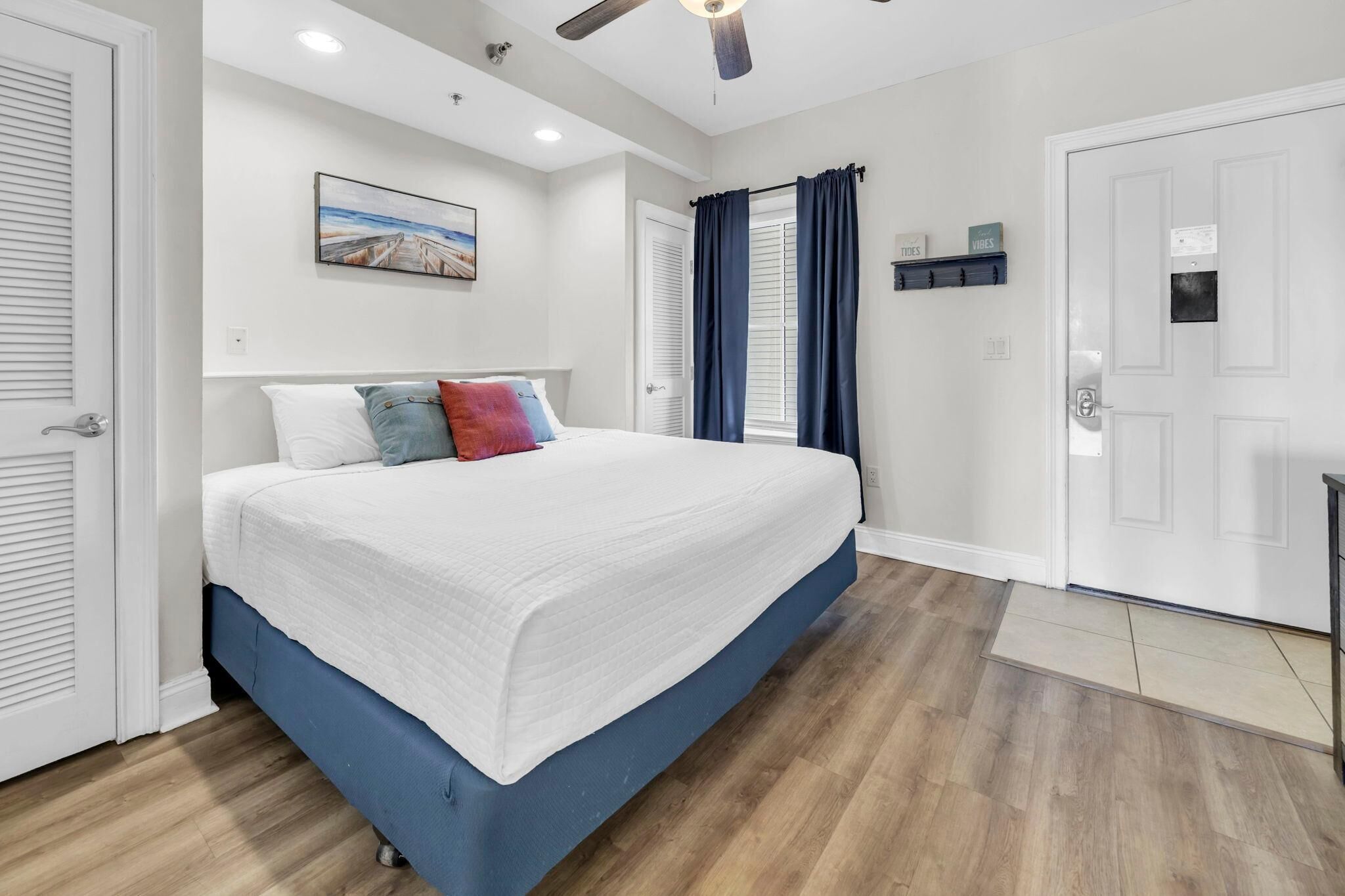 A bedroom with a bed, a ceiling fan, a window with curtains, and a door.