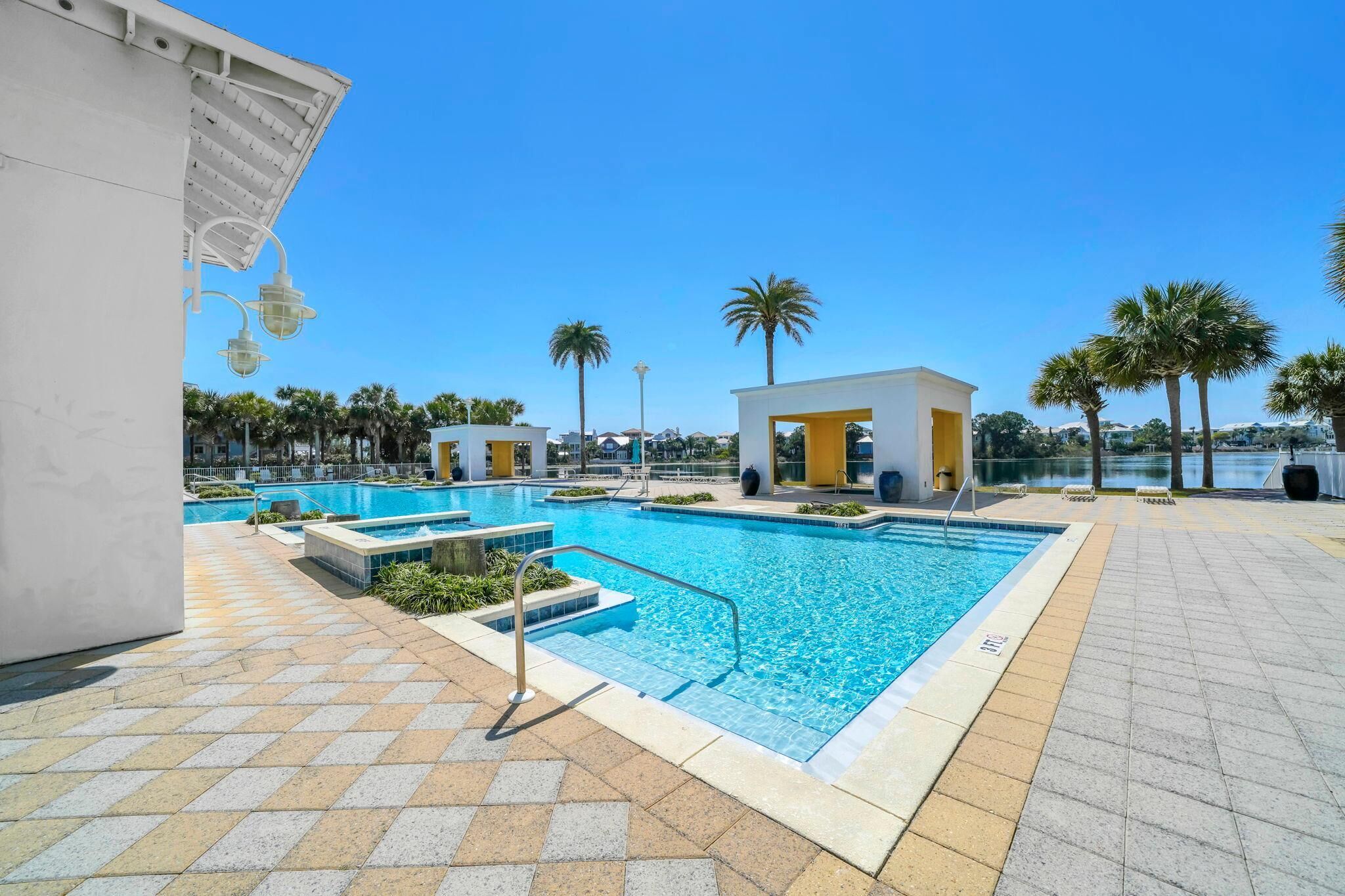 A swimming pool with a tiled deck, a small pavilion, and palm trees in the background.