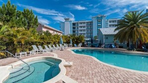 Piscina com espreguiçadeiras, palmeiras e um prédio de hotel ao fundo.