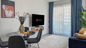 Een moderne woonkamer met een flatscreen televisie, een eettafel met stoelen, een bank en een groot raam met gordijnen.