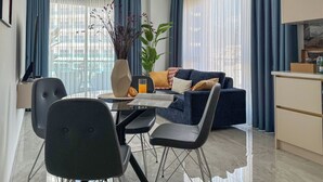 Een moderne woonkamer met een bank, eettafel, stoelen, een vaas met planten en een keukenhoek.