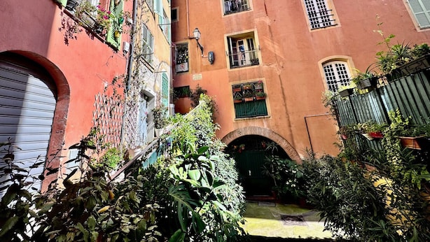 A narrow alleyway with buildings on either side, featuring balconies with plants and a small archway at the end. - Cocon du Senat 2 - Old Town (Niza)