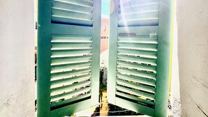A view through a pair of open shutters, revealing a building facade with horizontal lines and a visible window. - Cocon du Senat 2 - Old Town (Niza)