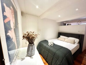 A bedroom with a bed, a bedside table with a vase, a wall with a poster, and a ceiling light. - Cocon du Senat 2 - Old Town (Niza)