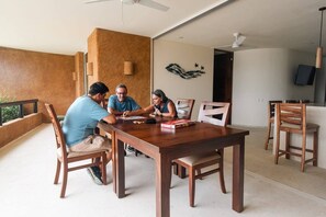 A dining area with a wooden table and chairs, a ceiling fan, and a wall-mounted artwork. - Luxury Livving Steps from La Ropa - 2Br 2 Bath (Zihuatanejo)