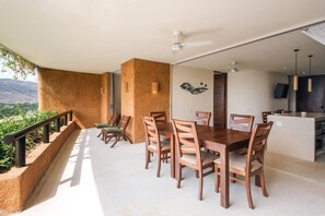 A dining area with a table and chairs, a ceiling fan, and a view of greenery. - Luxury Livving Steps from La Ropa - 2Br 2 Bath (Zihuatanejo)