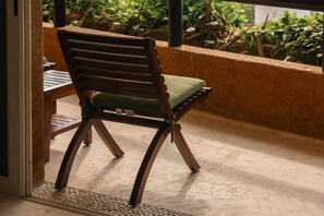 Una silla de madera con cojín, ubicada en un balcón con vistas a la vegetación.