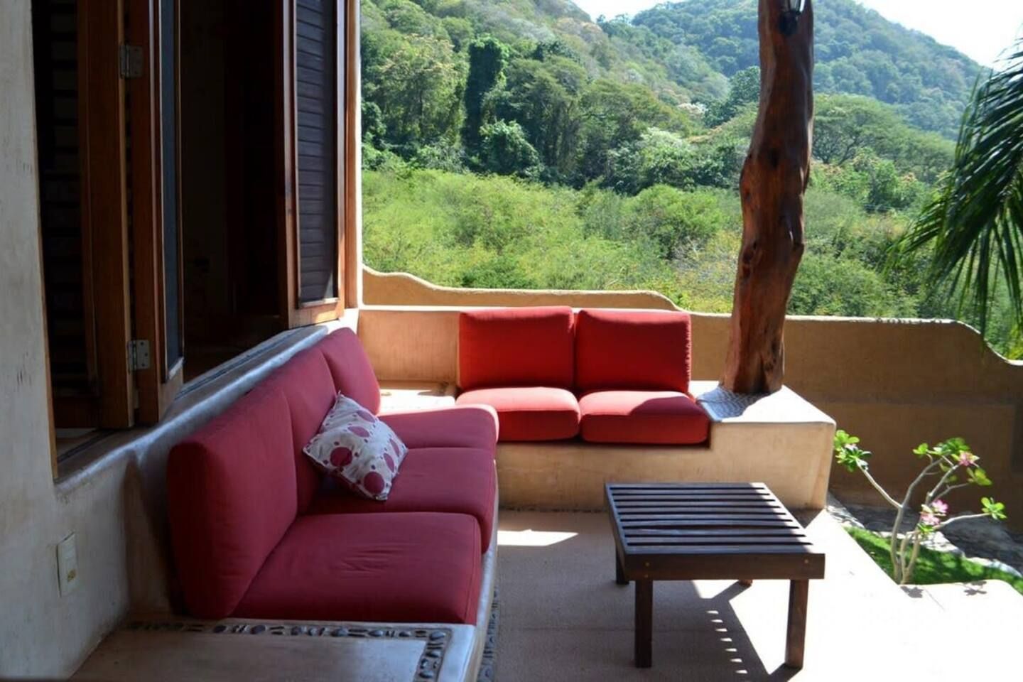 Un balcon avec un canapé rouge et une petite table, donnant sur un paysage verdoyant et luxuriant.