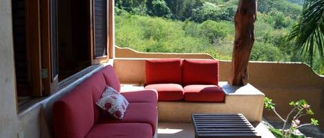 A balcony with a red sofa and a small table, overlooking a lush green landscape.