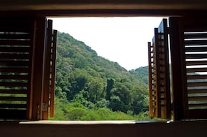 A view through open wooden shutters of a lush green hillside. - Luxurious Troncones Estate with 360 Views & Pool (Troncones)