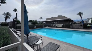 Une piscine entourée de palmiers et d’un bâtiment portant une enseigne, avec des chaises longues et des parasols à proximité.