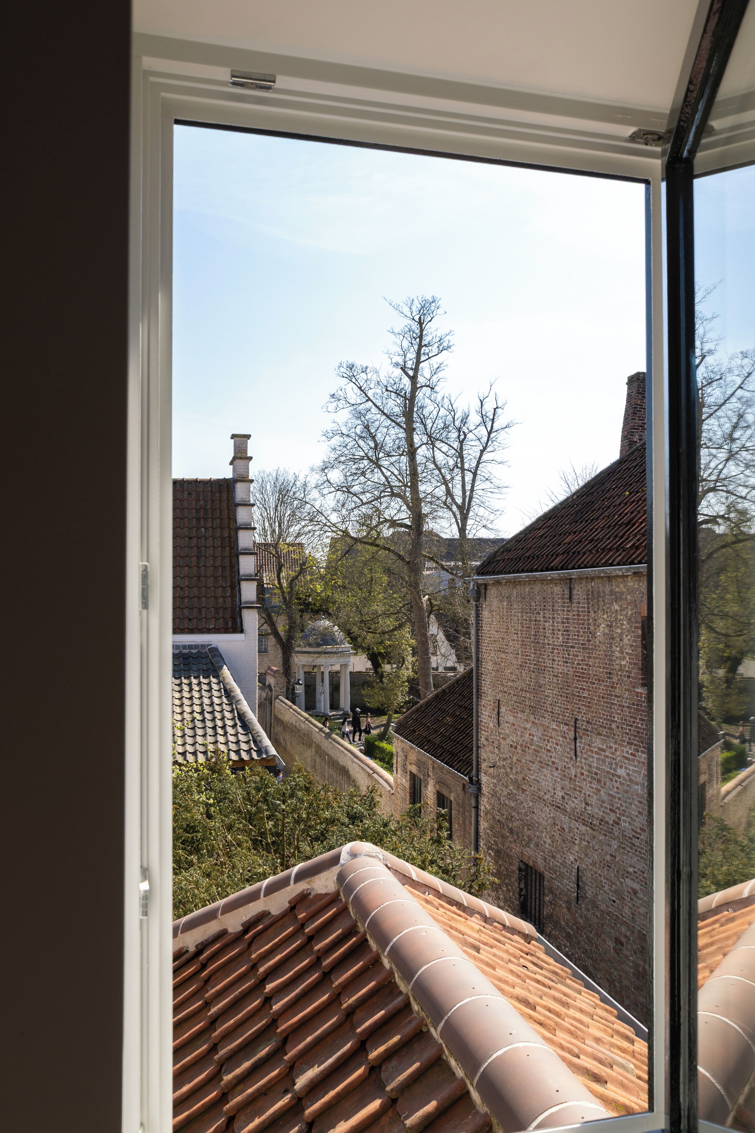 A view through a window of a building with a tiled roof, brick walls, and a clear sky.