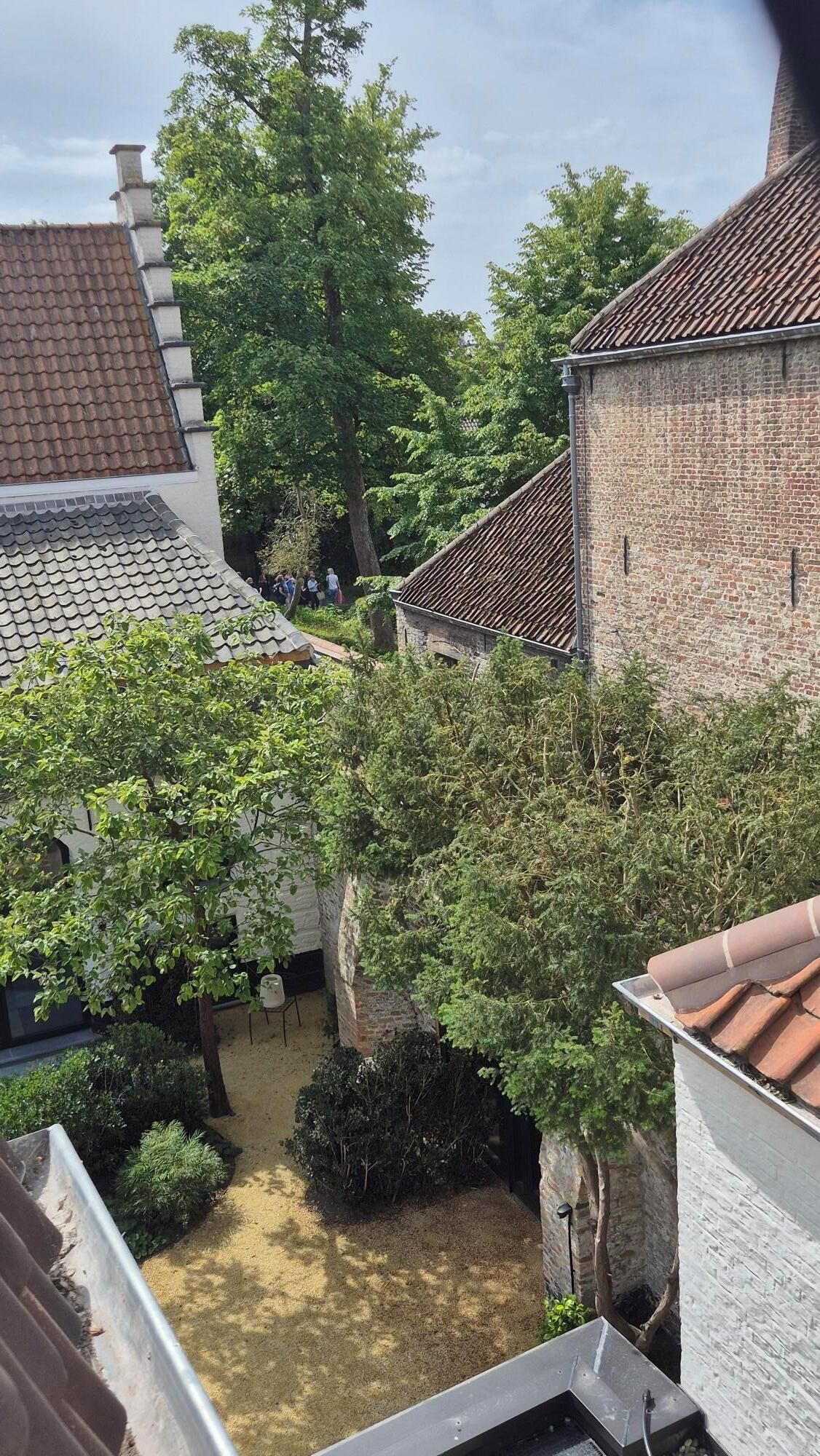 A courtyard with a brick building, a tiled roof, and lush greenery.