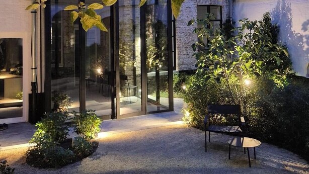 A modern building with a glass entrance, a gravel courtyard, and a bench. - Everelmus (Bruges)