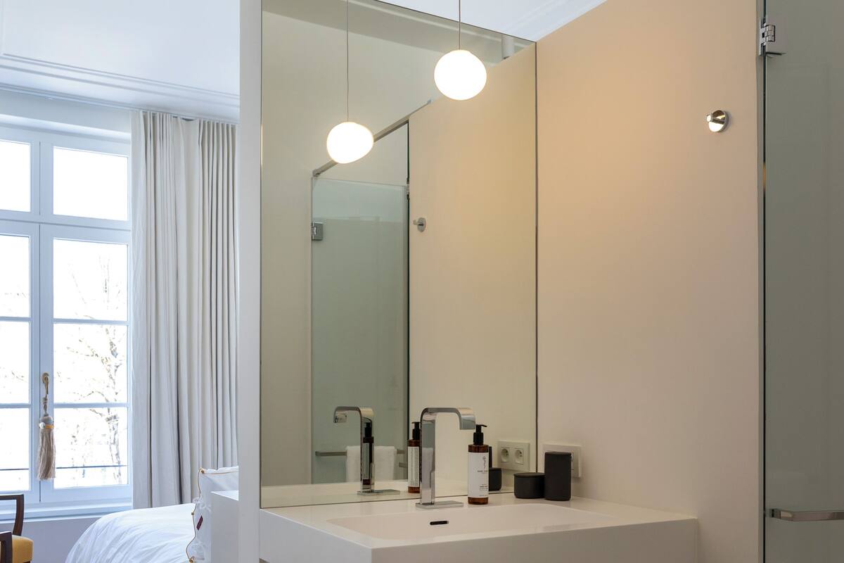 A modern bathroom with a large mirror, white sink, and wooden shelf.