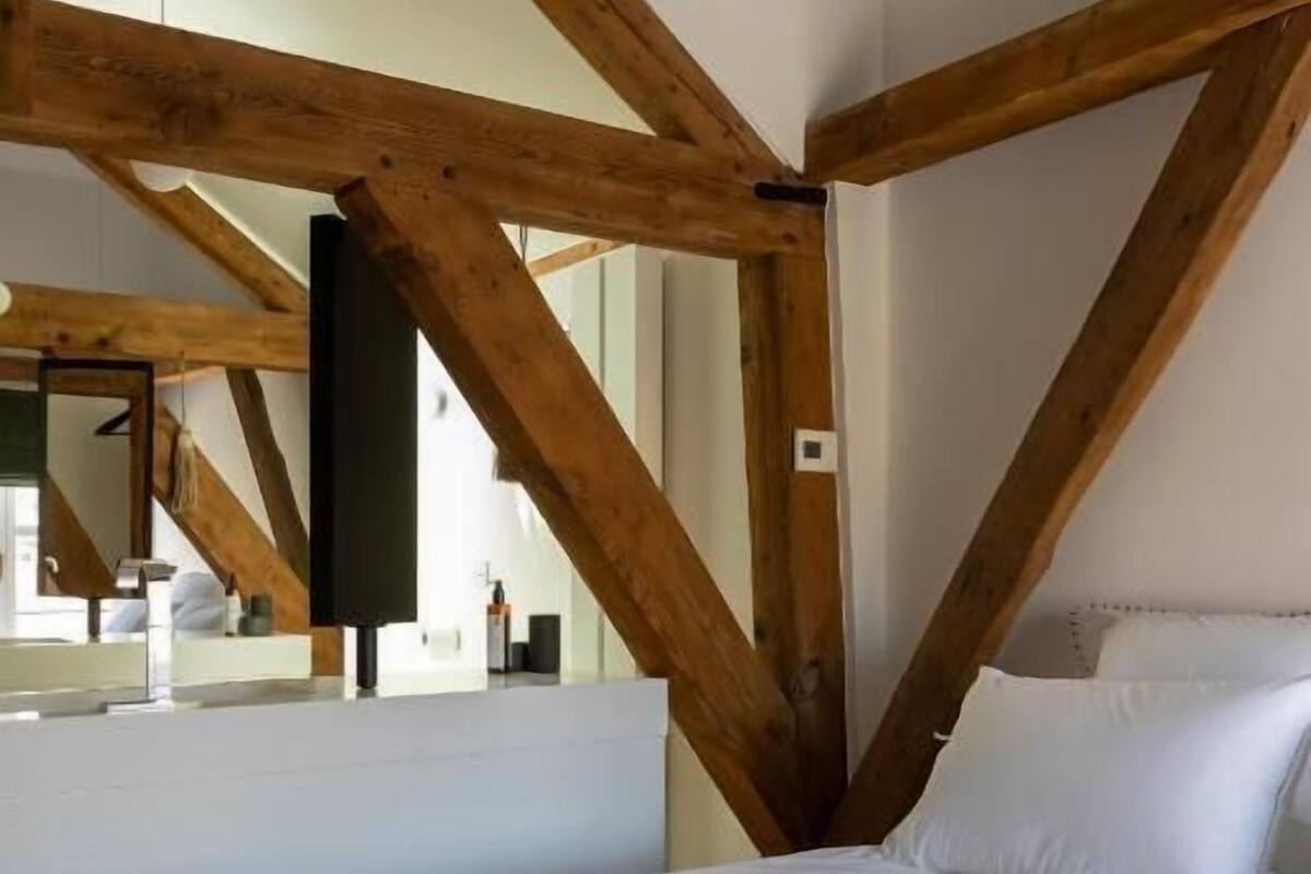 A bedroom with a large bed, wooden beams, a mirror, and a white wall.