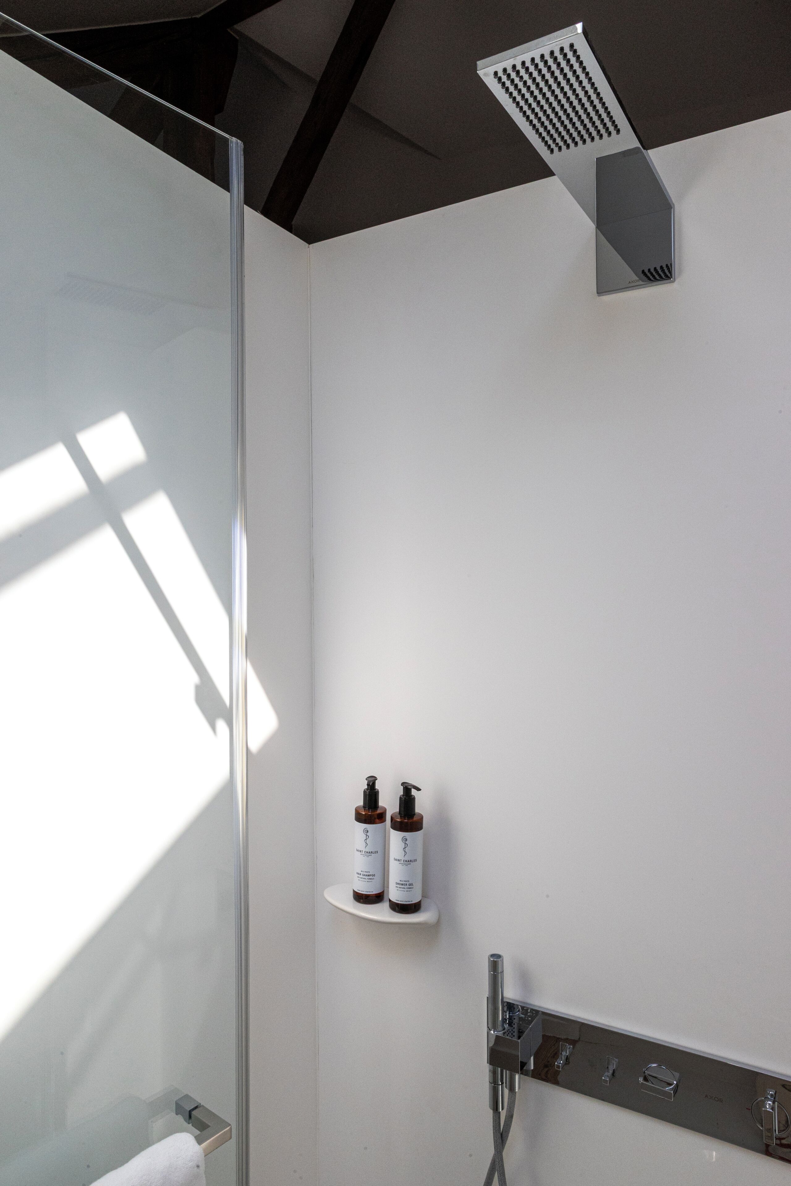 Un baño moderno con cabina de ducha de vidrio, un perchero, una repisa con artículos de aseo y un cabezal de ducha.