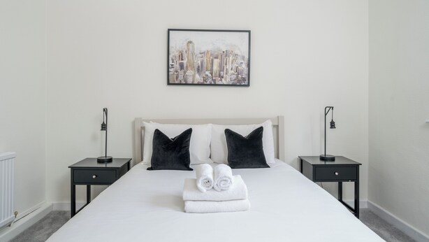 Een hotelkamer met een groot bed, twee nachtkastjes, een kunstwerk met een stadsgezicht in een lijst en een radiator.