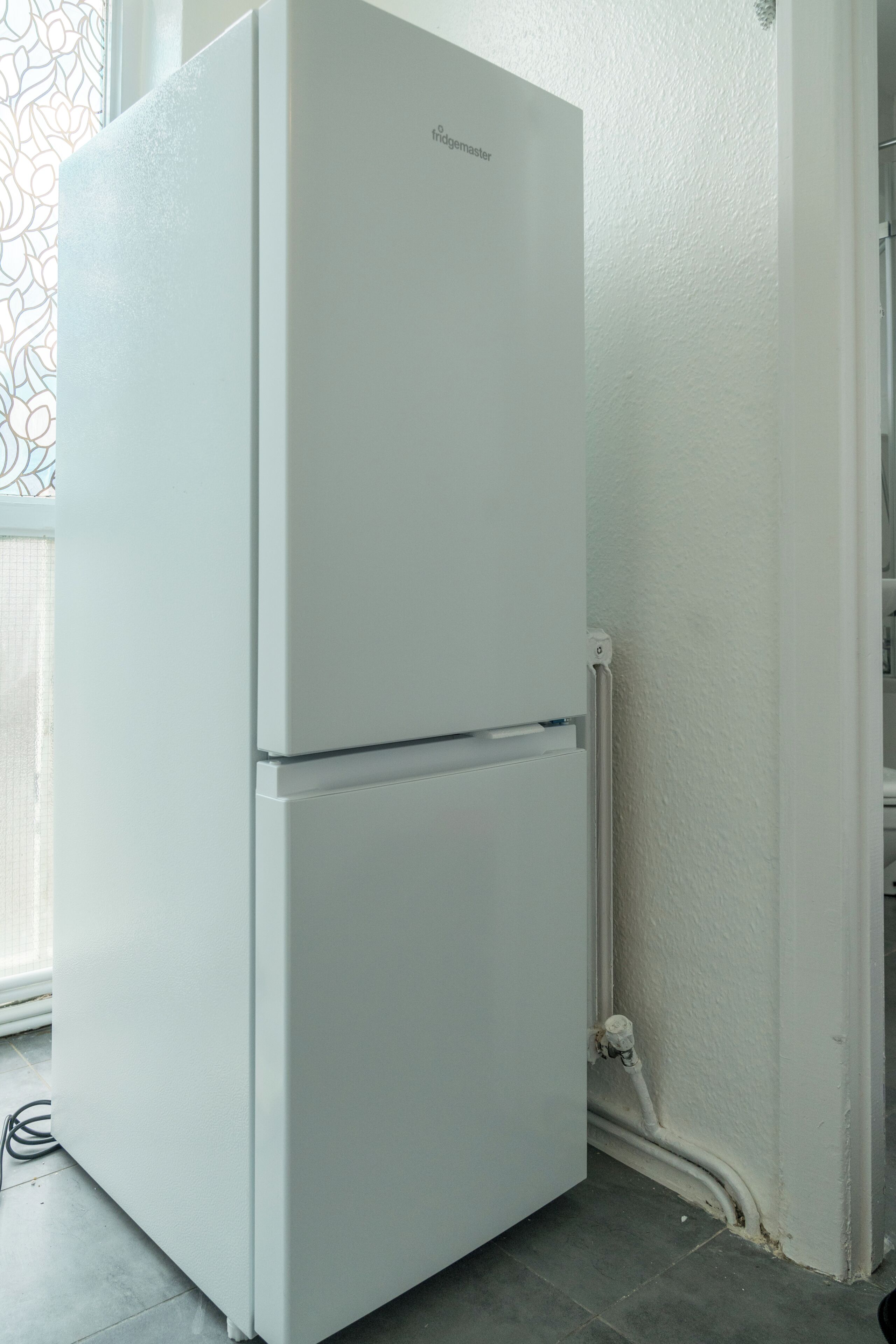 Un refrigerador blanco en una habitación con piso de baldosas y pared blanca.