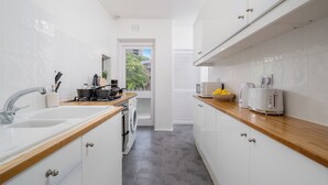 Een moderne keuken met witte kastjes, een houten aanrechtblad en uitzicht door een open deur.