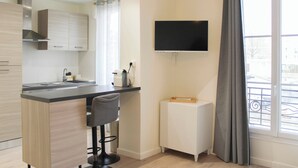A modern kitchen with a built-in island, a flat-screen TV, and a window with a view of the outside. - Bright studio apartment on the outskirts of Paris (Clichy)