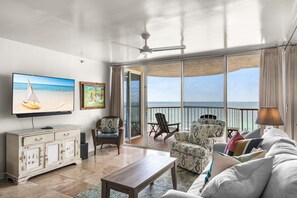 A living room with a television, a sofa, a coffee table, a cabinet, and a balcony with a view of the ocean. - Wonderful Gulf Front Condo at Hidden Dunes (Miramar Beach)