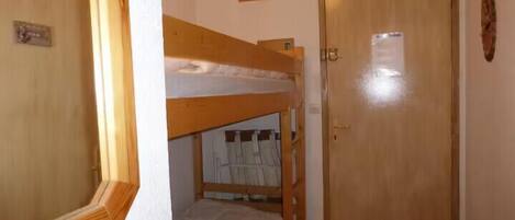 A room with a bunk bed, a wooden door, and a small picture on the wall.