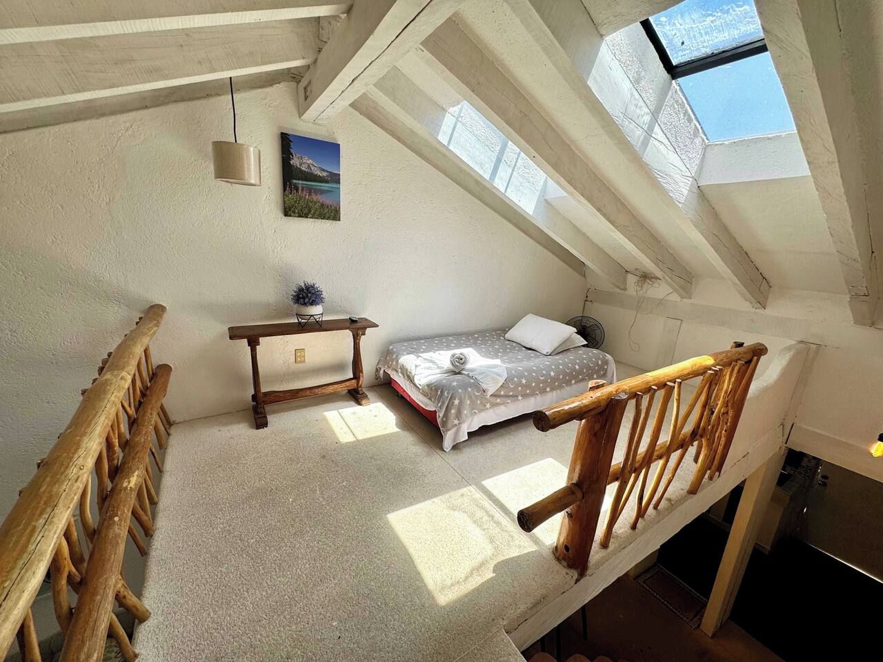 Een kamer met hoge plafonds, een dakraam, een bed, een houten bank en een kleine tafel.