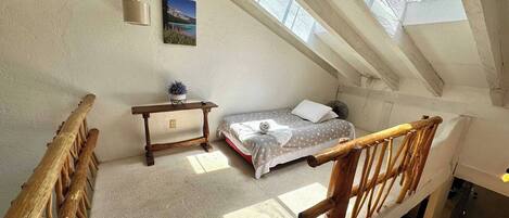 Een kamer met hoge plafonds, een dakraam, een bed, een houten bank en een kleine tafel.