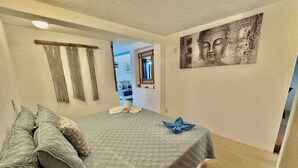 Une chambre à coucher avec un lit, des oreillers, une œuvre d’art accrochée au mur et une porte donnant sur une autre pièce.