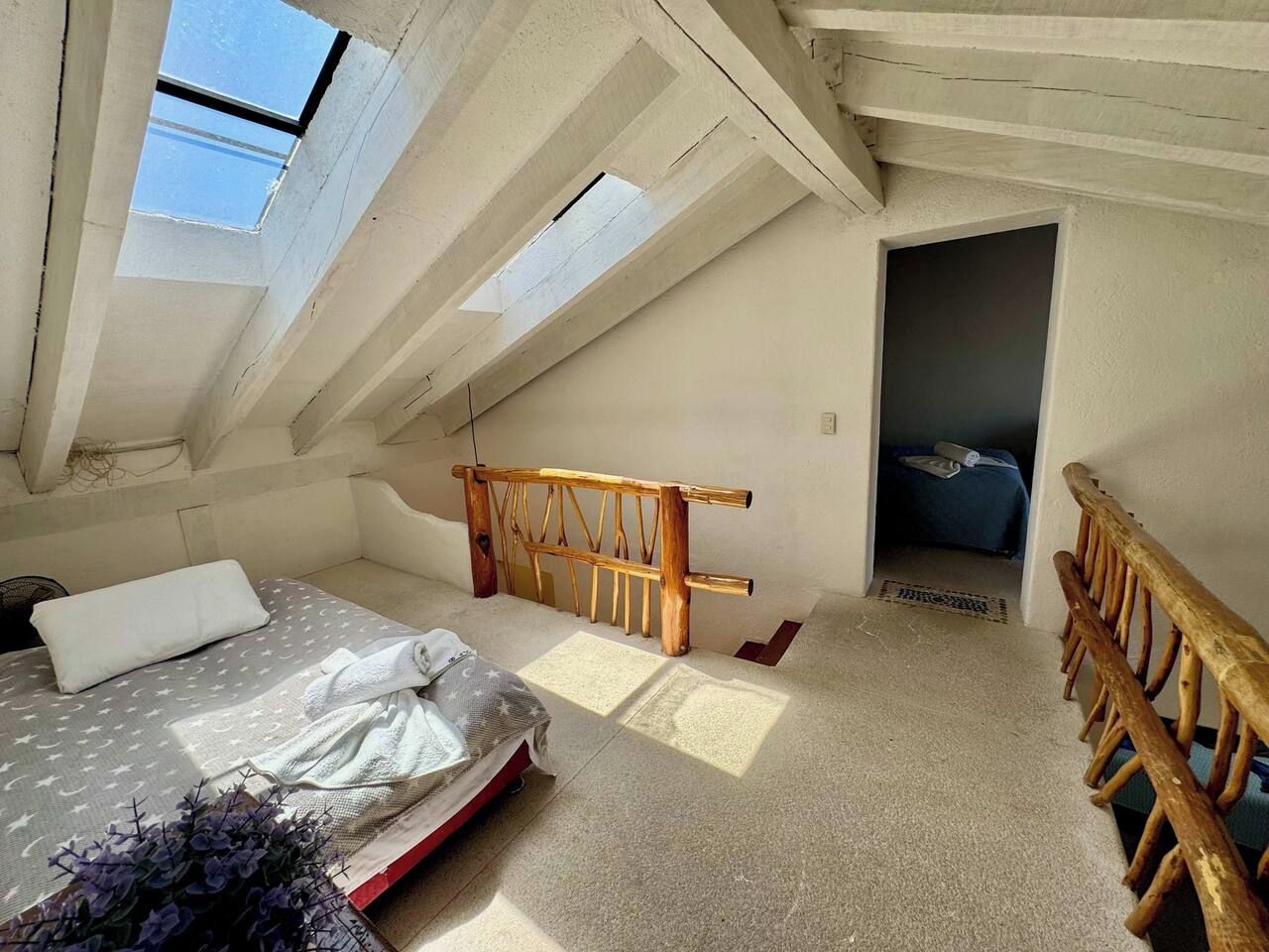 Una habitación con cama, tragaluces, cabecera de madera y un pequeño vestíbulo.