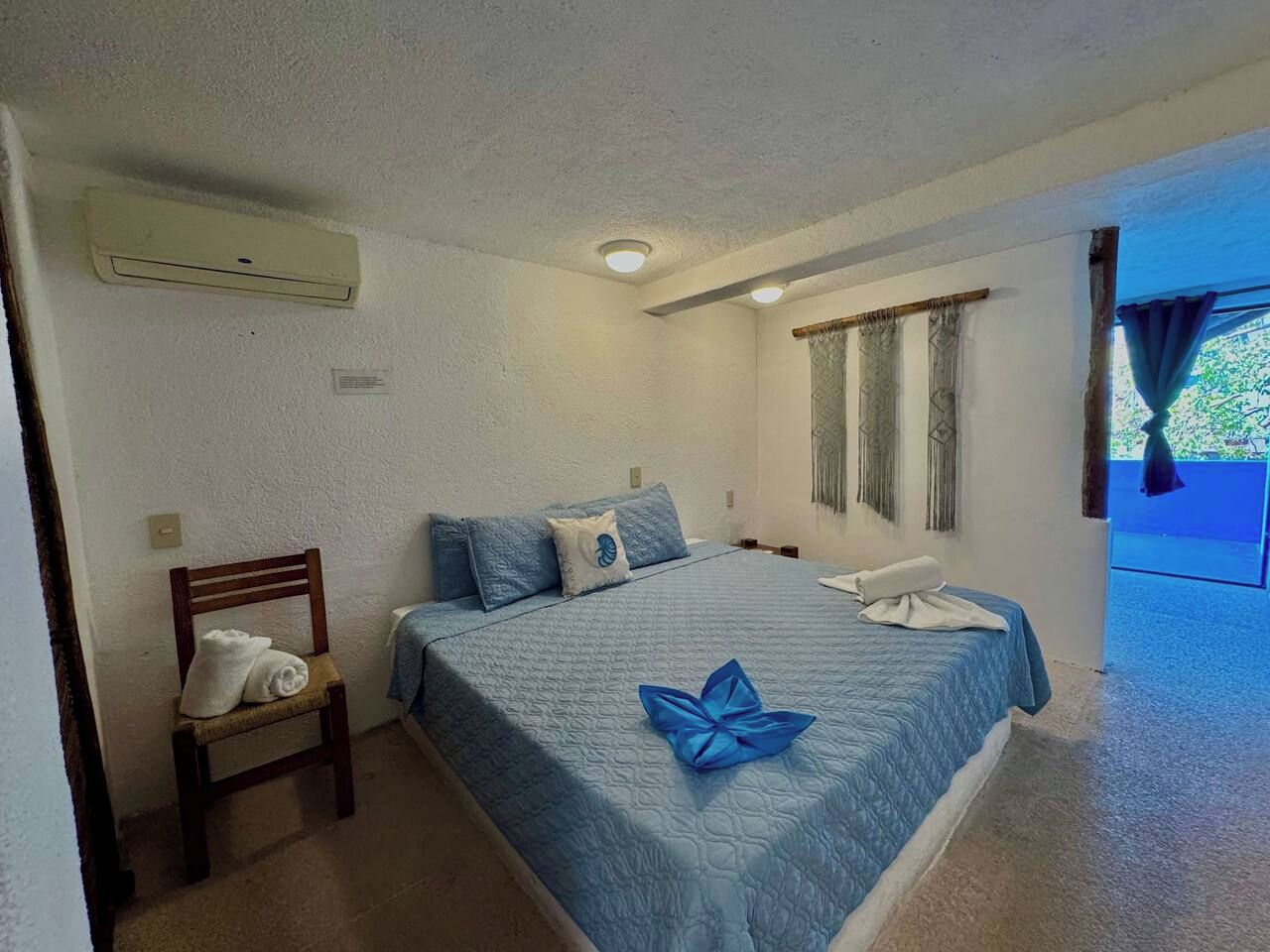 A bedroom with a bed, a chair, a window with curtains, and an air conditioning unit.