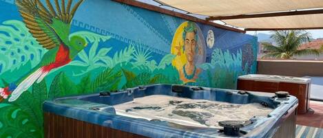 A hot tub under a shaded area with a mural of a bird and a face.