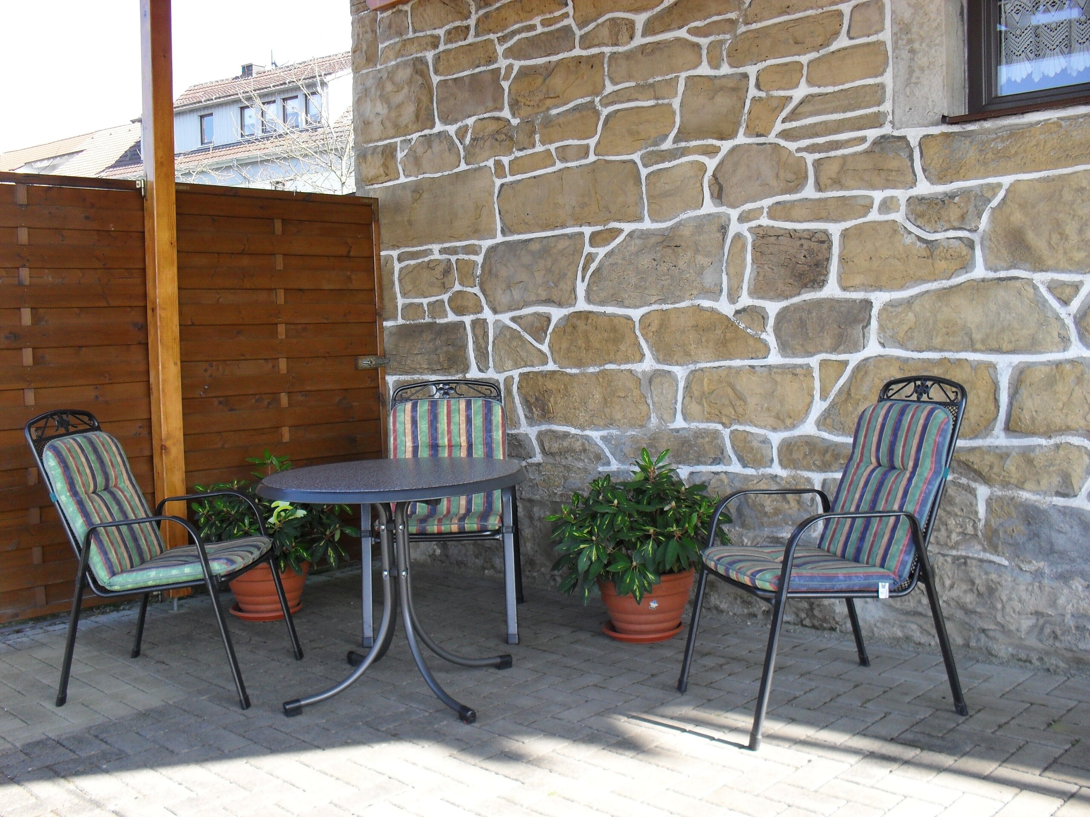 Een terras met een stenen muur, een houten poort en een tafel met stoelen.