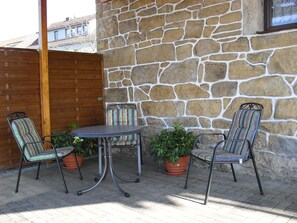 Une terrasse avec un mur en pierre, une porte en bois et une table avec des chaises.