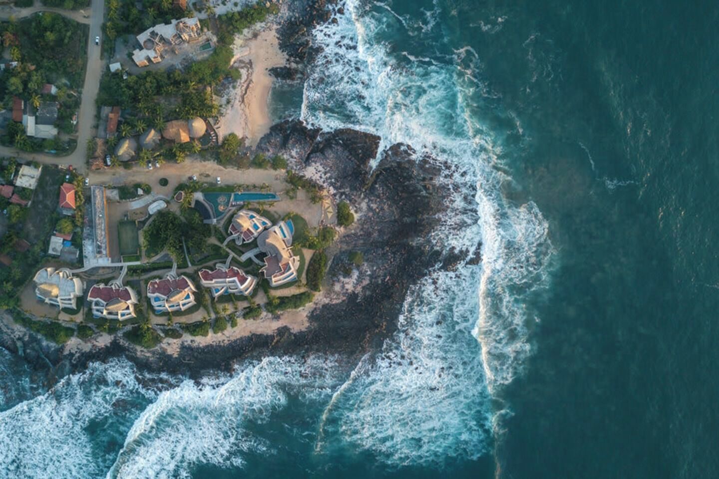An aerial view of a coastal resort with multiple buildings, a beach, and rocky shoreline.