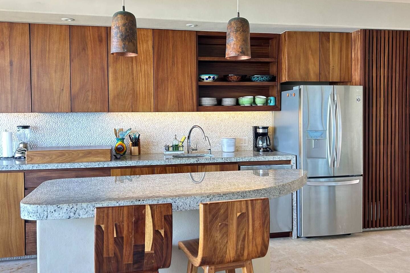 Une cuisine moderne avec des meubles en bois, un réfrigérateur en acier inoxydable et un plan de travail en granit.