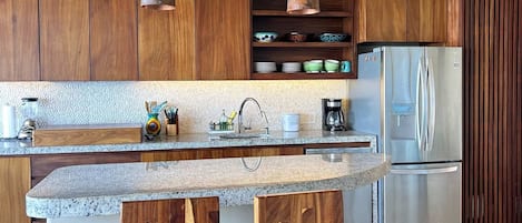 A modern kitchen with wooden cabinets, a stainless steel refrigerator, and a granite countertop.