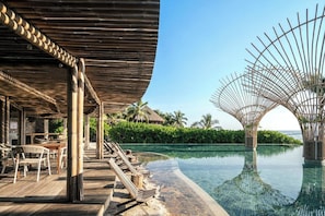 A wooden deck with lounge chairs and a pool with a clear view of the ocean.
