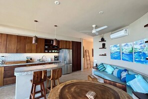 A modern kitchen with wooden cabinets, a central island, and bar stools. There is a refrigerator, a coffee maker, and a ceiling fan. - Luxury Sofia 6 in luxury condo (La Majahua)